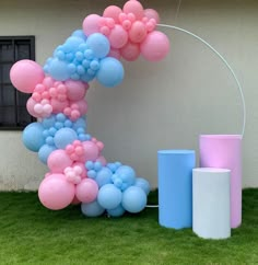 a balloon arch with pink, blue and white balloons on the grass next to it