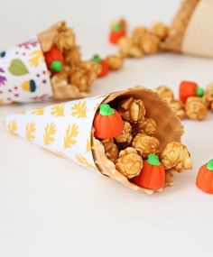 a paper cone filled with candies and nuts on top of a white table next to small pumpkins