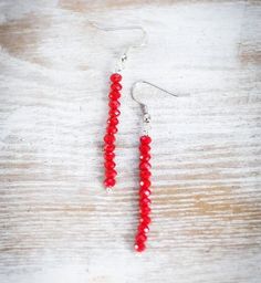 the red beaded earrings are hanging from silver hooks on a white wooden surface,