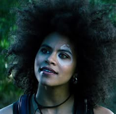 a woman with an afro standing in front of trees