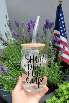 a person holding up a glass with the words shut put cape on it in front of some flowers