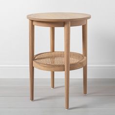 a round wooden table with a wicker basket on the bottom and one shelf below it