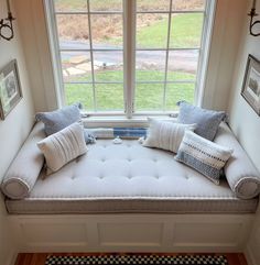 a window seat in the corner of a room with pillows and pictures on the wall