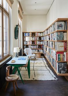 a room filled with lots of books on shelves next to a table and chair in front of a window