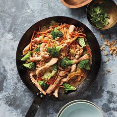 a wok filled with chicken, broccoli and carrots on top of a table