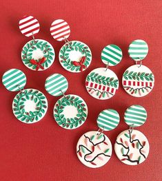 twelve christmas themed earrings on a red surface with white and green stripes, decorated with holly wreaths