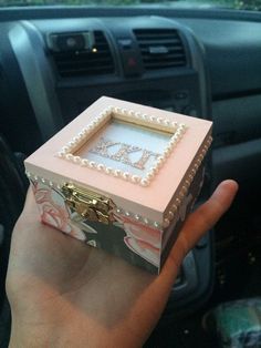 a hand holding a pink and white box with pearls on the inside, in front of a car