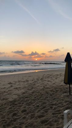 the sun is setting at the beach with chairs and umbrellas