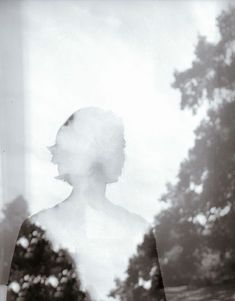 a black and white photo of a woman with trees in the background