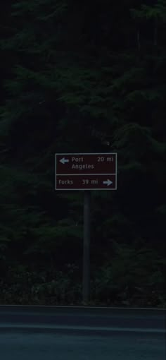 a street sign sitting on the side of a road next to some tall green trees