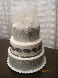 a three tiered cake with white feathers on it's top and silver trim