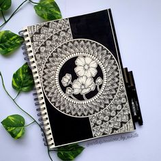 a black and white notebook sitting on top of a table next to some green leaves