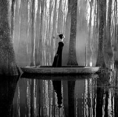 a woman standing in a boat on top of a body of water surrounded by trees