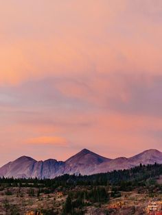 the sky is pink and purple as the sun sets in the distance behind mountains with trees on each side