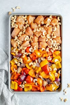 a pan filled with chicken and vegetables on top of a white table cloth next to cashews