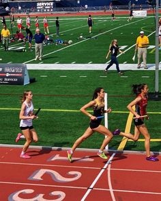 three girls running in a race on a track with people watching from the sidelines