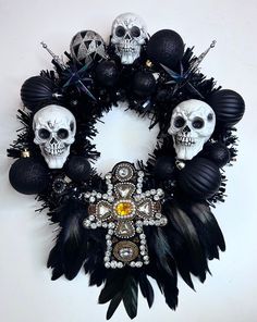 a wreath decorated with skulls and feathers on a white wall in the shape of a cross