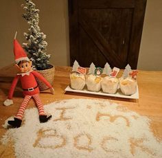 an elf sitting on top of a table next to some cookies and marshmallows