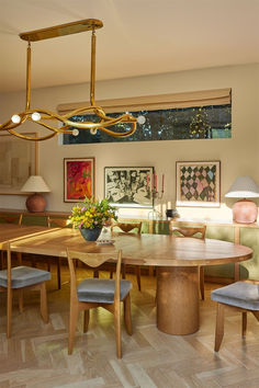 a dining room table surrounded by chairs and art work on the wall above it is a chandelier that hangs from the ceiling