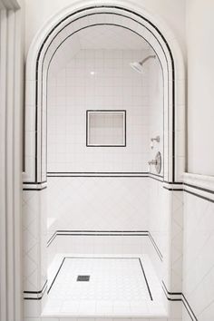 a bathroom with white tile and black trim around the shower area, along with an arched doorway