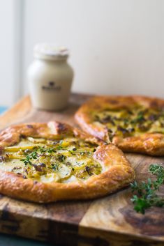 two pizzas sitting on top of a wooden cutting board next to a jar of mayonnaise