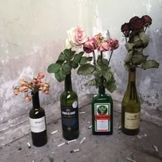 three wine bottles with flowers in them sitting next to each other on the ground near a wall