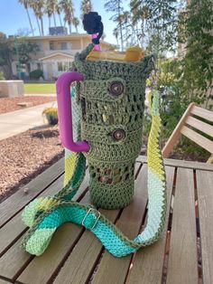 a crocheted coffee cup sitting on top of a wooden table next to a purple handle