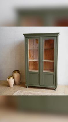 a green cabinet sitting on top of a wooden floor next to a vase and pot