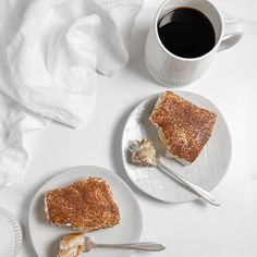 two plates with slices of cake on them next to a cup of coffee and napkins