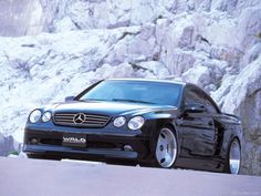 a black mercedes cls parked in front of a rocky mountain side with snow on the ground