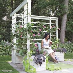 a woman sitting on top of a planter next to a white fence with pink flowers