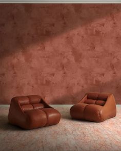 two brown leather chairs sitting in front of a pink wall