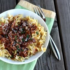 a white bowl filled with pasta and meat on top of a green napkin next to silverware