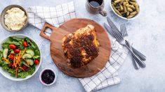 a wooden cutting board topped with meat next to bowls of salad