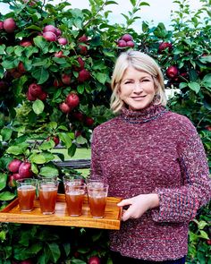 a woman standing in front of an apple tree holding a tray with apples on it