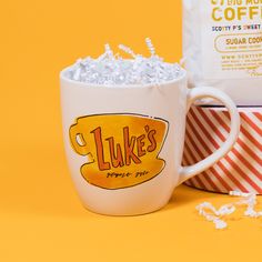 On a sunny mustard background sits a mug with white crinkle in it. This Gilmore Girls inspired mug has an illustration of Luke's Gilmore Girls coffee mug in colors of sunny mustard, orangey-red, and black. Gilmore Girls Theme Song, Luke's Coffee, No Cell Phone Sign, Honorary Gilmore Girl, Gilmore Girls Luke, Lukes Diner, Coffee Gifts Box, Gilmore Girls Fan, Kitchen Candles