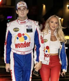 a man and woman dressed in racing gear walking down the street holding hands with each other