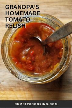 a jar filled with homemade tomato relish sitting on top of a wooden table next to a spoon