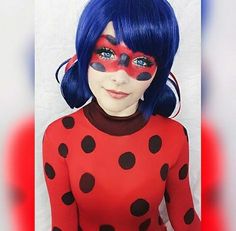 a woman with blue hair wearing a red and black polka dot costume, her face painted like a ladybug