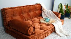 a brown couch with a white blanket on it and a blue cup sitting on top of it