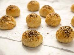 rolls with sesame sprinkled on them sitting on a piece of parchment paper