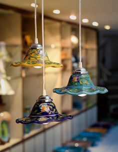 three colorful glass bells hanging from the ceiling in a store or restaurant with other items on display behind them