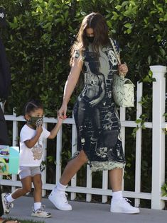 a woman holding the hand of a small child as they walk past a white picket fence