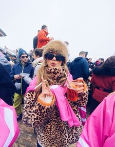 a woman wearing sunglasses and a leopard print coat is holding a drink in her hand