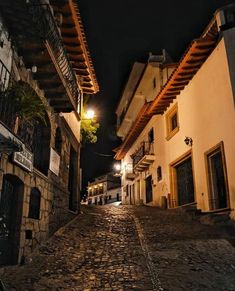 an empty cobblestone street at night with lights on and buildings in the background