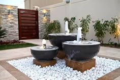 two black bowls with candles in them sitting on top of some rocks and gravel next to a house