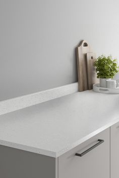 a white counter top with a plant and cutting board sitting on it's side