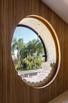 a circular window in the side of a wooden wall with palm trees and water outside