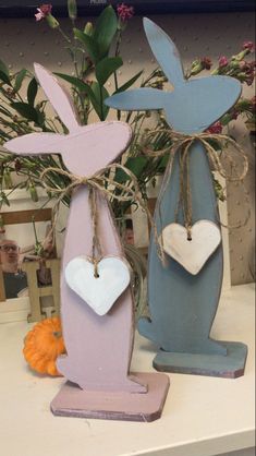 two wooden rabbits with hearts attached to them on top of a table next to flowers