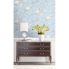 a white vase with flowers sitting on top of a wooden dresser next to a lamp